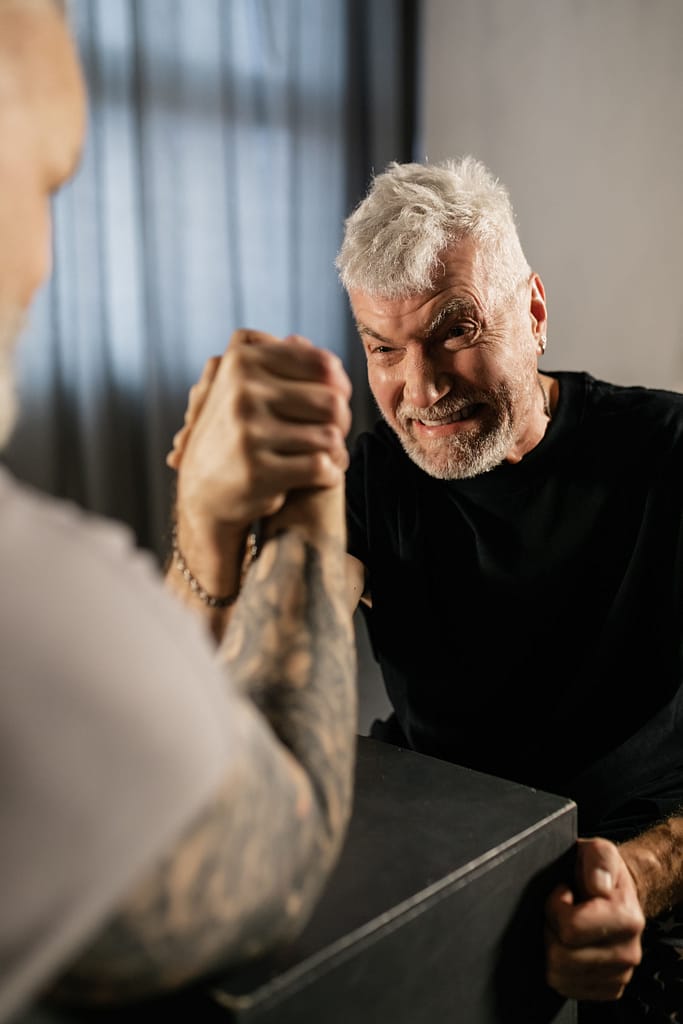 Two middle-aged men engaged in a competitive arm wrestling match, with one focused and straining against the other.