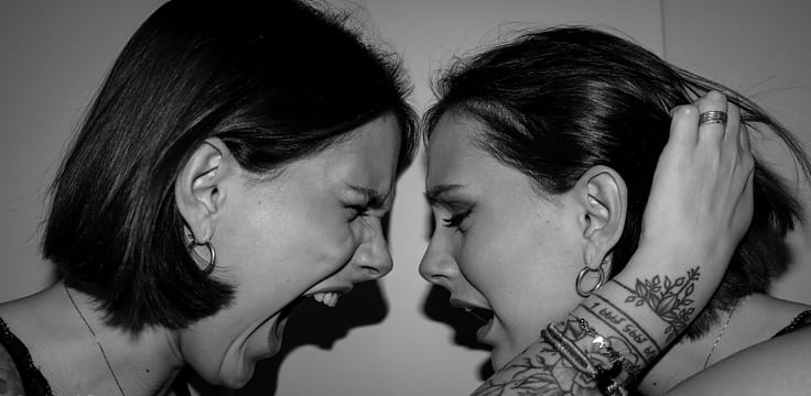 Two women facing each other, aggressively screaming with intense expressions in a high-contrast black and white image.