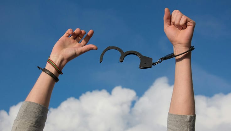 Hands breaking free from handcuffs against a bright blue sky with clouds.